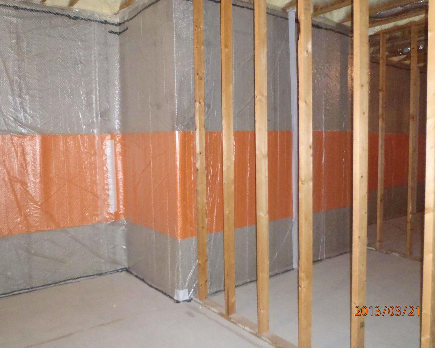 Unfinished basement with exposed framing, concrete floor, and insulated walls with orange vapor barrier.
