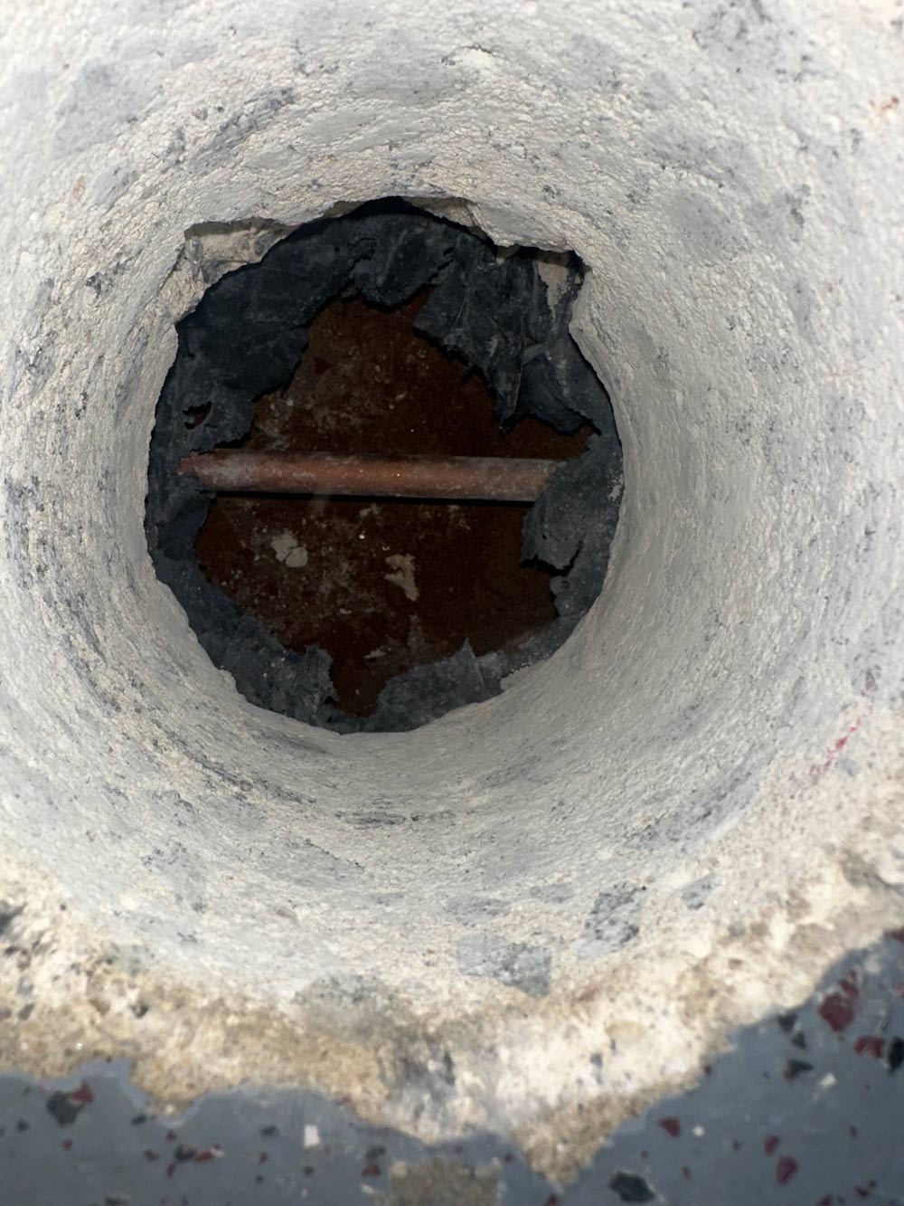 A concrete pipe or hole with a rusty metal rod running horizontally inside it.