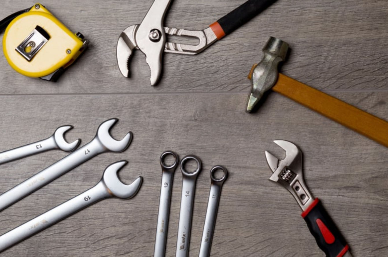 Various hand tools including wrenches, pliers, a hammer, and a tape measure on a wooden surface.