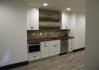 Modern kitchen with white cabinets, brick backsplash, wood counters, and stainless steel appliances.