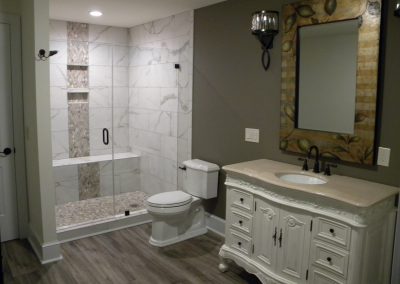 Modern bathroom with glass shower, white vanity, ornate mirror, and wood-look flooring.
