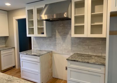 Unfinished kitchen with white cabinets, gray countertops, and a stainless steel range hood.