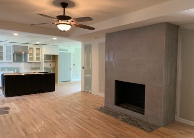 Open-concept living area with a modern fireplace, ceiling fan, and a kitchen with unfinished cabinetry.