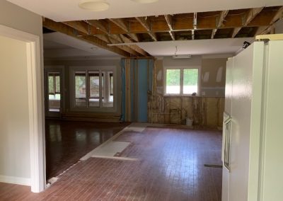 Partially renovated room with exposed ceiling beams, unfinished walls, and a refrigerator on the right.