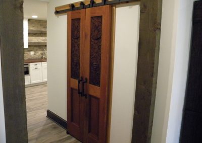 Wooden sliding barn door with decorative carvings, partially open to reveal a kitchen with white cabinets.