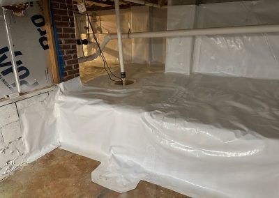 Clean crawl space with white vapor barrier, exposed pipes, and brick wall in background.