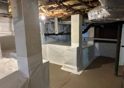 A basement with exposed pipes and columns, partially covered in white plastic sheeting and insulation overhead.