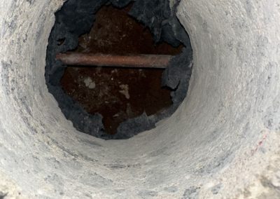 A close-up view of a concrete pipe or hole with a rusted metal rod running across the center inside.