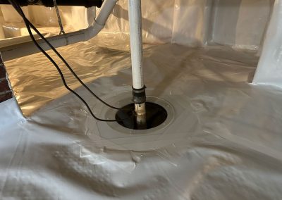 A sump pump installed in a basement with a white vapor barrier covering the floor and walls.