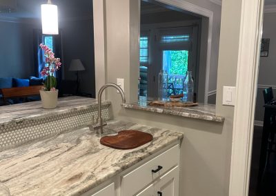 Kitchen with white cabinets, marble countertop, and a passthrough window overlooking a dining area.