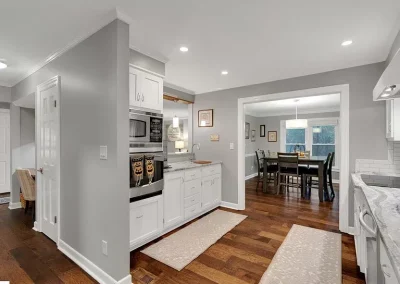 Modern kitchen with white cabinets, stainless appliances, and a view into a dining room with wood flooring.